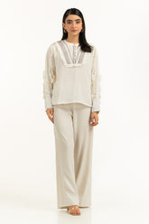 Woman wearing a white blouse with lace details and beige pants on a white background